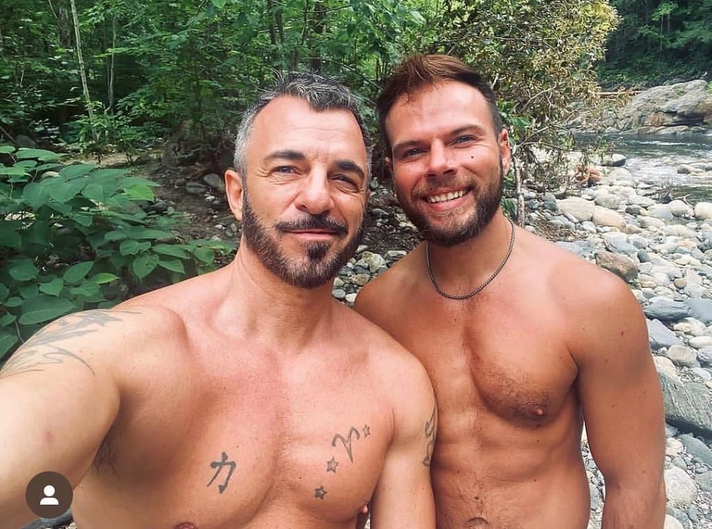 Two smiling shirtless visitors selfie on smooth river stones at Rock River, Vermont — clear water and green forest