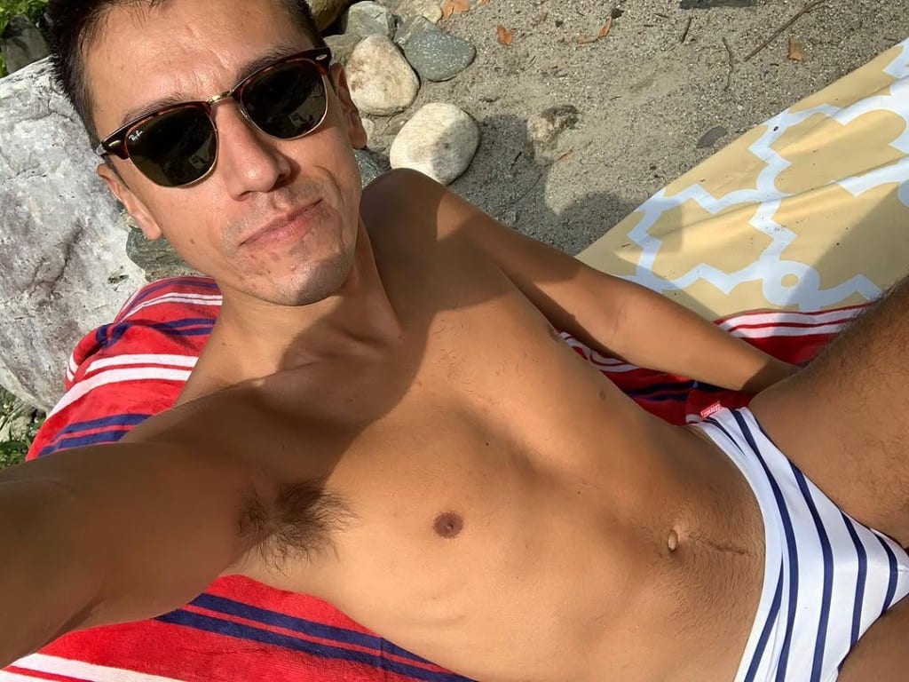 Visitor relaxing on a red striped towel on sand and river stones at Rock River, Vermont — sunglasses, sunny riverbank