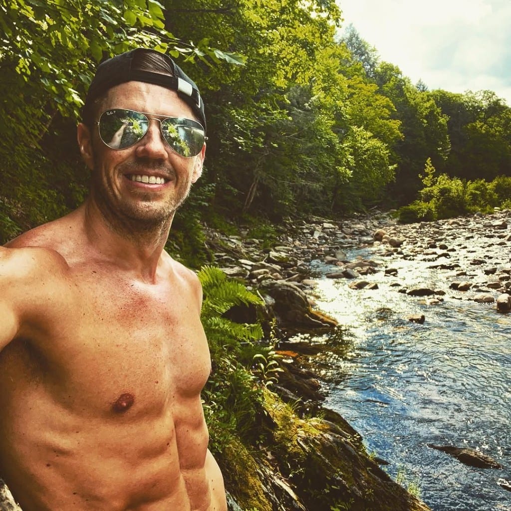 Visitor selfie with a sunlit rocky Rock River valley behind — sparkling water, ferns, and summer forest in Windham County, Vermont
