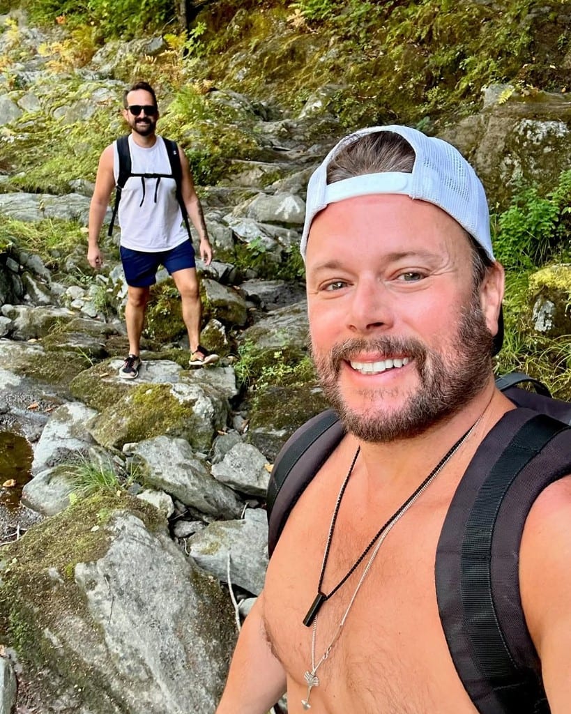 Rock River — trail selfie on the rocks Two visitors on a mossy rocky trail at Rock River, Vermont — hiking selfie, bright forest, shirts and packs, genuine smiles